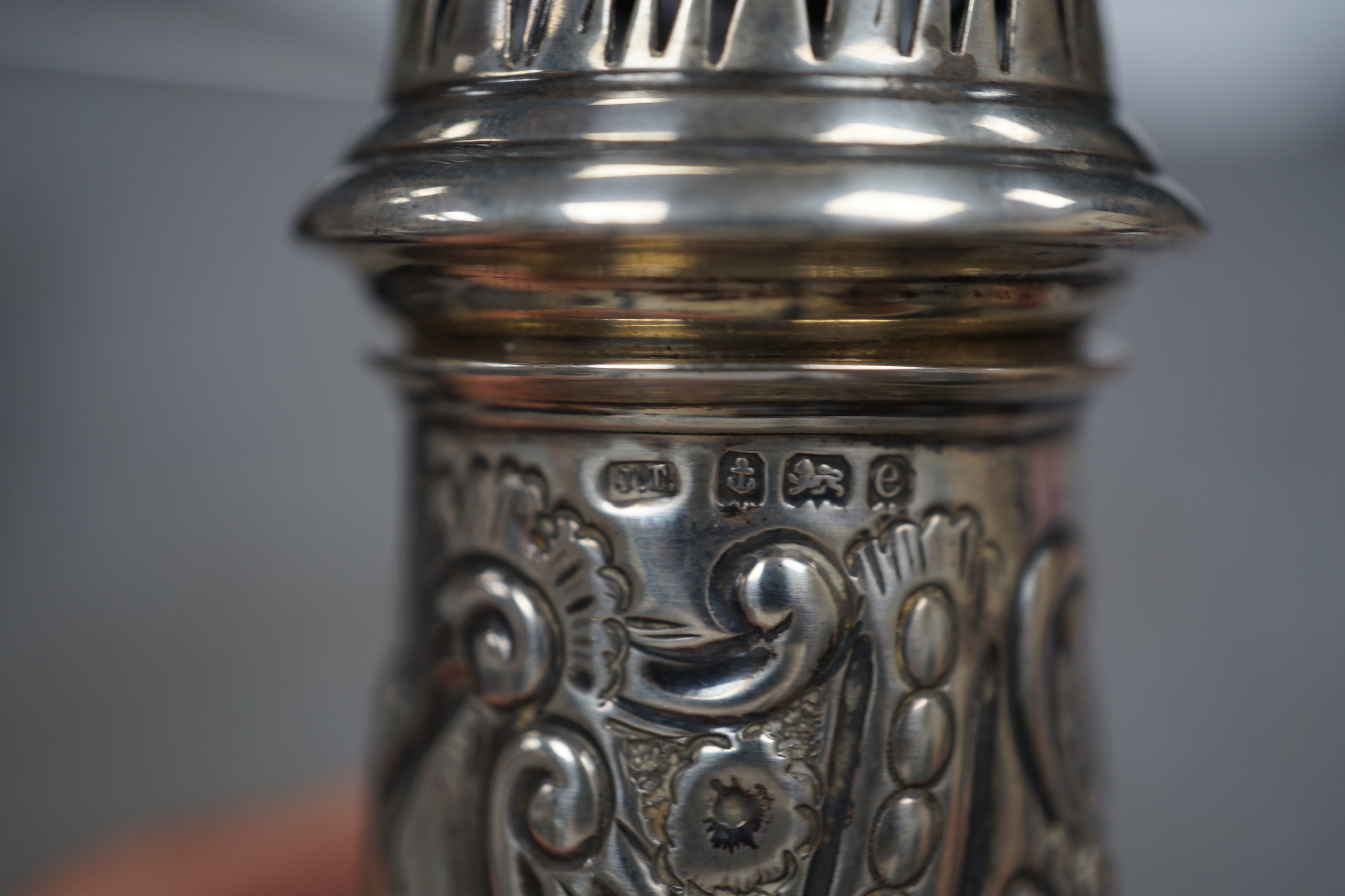 An Edwardian embossed silver sugar caster, Birmingham, 1904, 17.6cm and white metal cake basket stamped 'silver'.